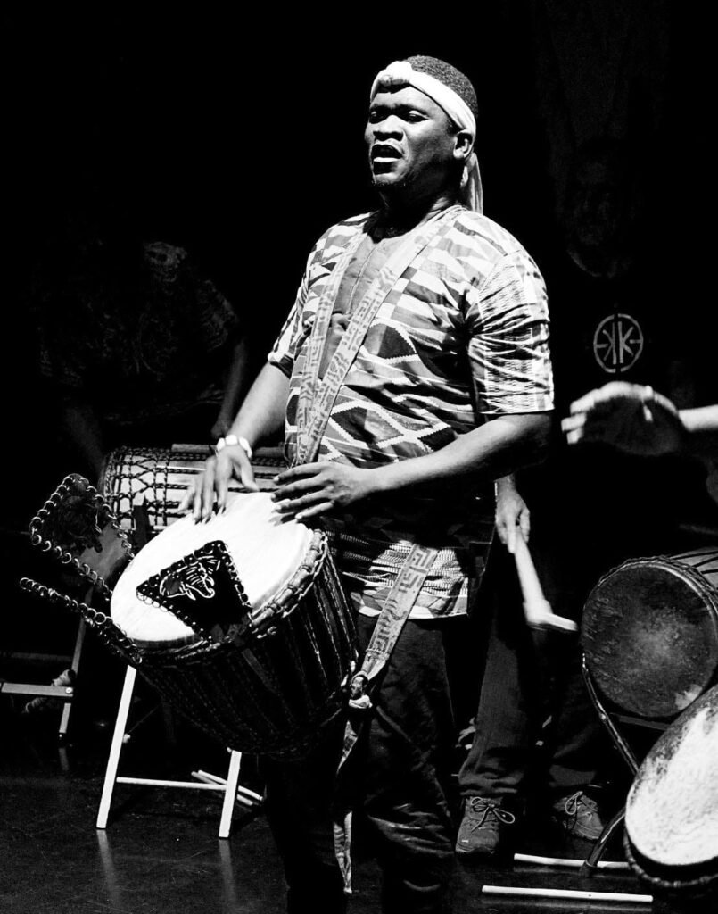 Billy Konaté spielt Djembe in einer Schwarz-Weiß-Aufnahme
