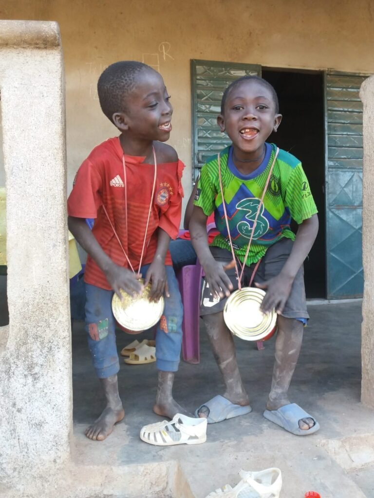 Zwei Kinder in Guinea musizieren gemeinsam mit einfachen Blechinstrumenten